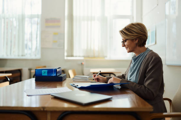 istock Smiling female teacher writing her plans in the classroom. 2147679978