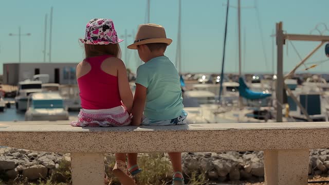 Children are sitting on the stone and looking at the bay with yachts