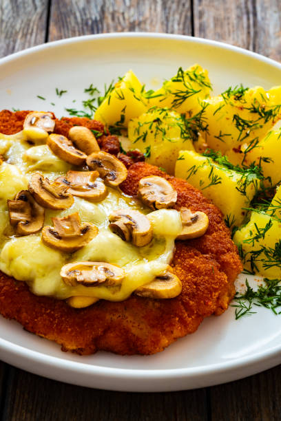 istock Breaded seared chicken cutlet with cheese, white mushrooms and boiled potatoes on wooden table 2147680107