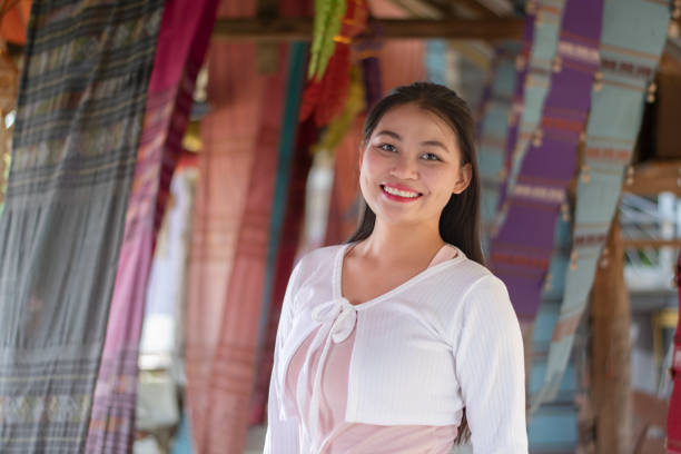 Asian young adult woman holds woven fabric which was decorated on ceiling of local cafe for tourist watching and taking photos, soft focus, happiness of humans concept.