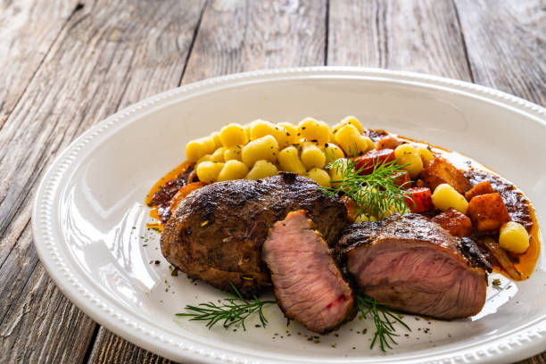 baked pork cheeks in sauce with gnocchi and vegetables in sauce on wooden table - steak plate gourmet beef imagens e fotografias de stock