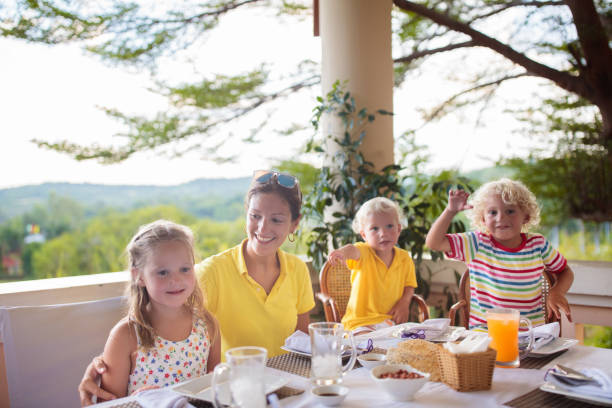 Family having dinner on outdoor patio. Mother and kids eating breakfast or lunch on a rooftop terrace in tropical resort. Garden and backyard dining area. Children eat outdoors.