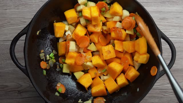 Top view pumpkin slices poured into vok pan with stewed vegetables