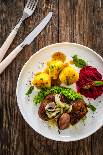 Baked pork cheeks with boiled potatoes and beetroots on wooden background