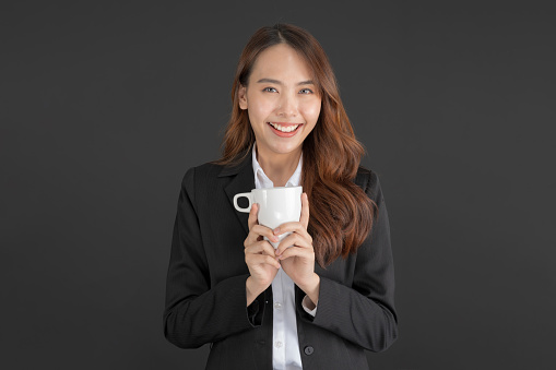 Business woman wearing a black suit Standing with a cup of coffee on a black background.