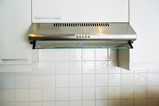 Picture of a wall-mounted exhaust hood placed above an electric stove for home kitchen appliances.
