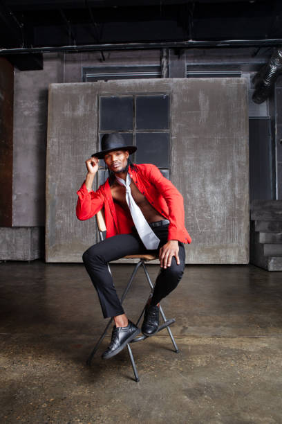 istock Contemporary African American man, actor or dancer sits on a stool on stage, dressed in a red shirt and a hat 2147685037