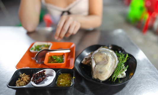 Local raw oyster with thai style seafood sauce. People traveling from tasty guide tour at China town asia street food market. Bangkok, Thailand