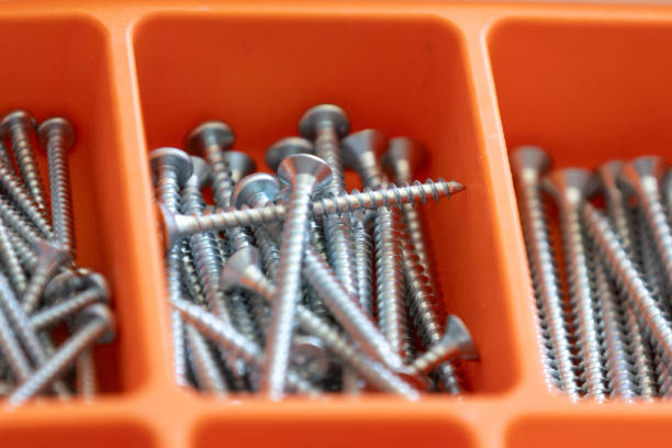 Collection of nails, thumb nails, screws, plastic and bolts in plastic box on the wooden table