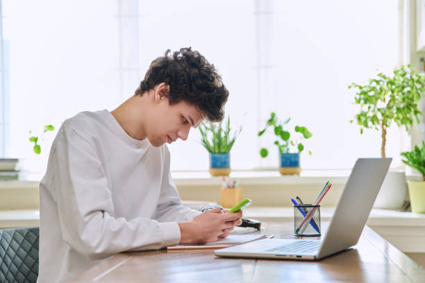 istock Young guy student using smartphone, sitting at his desk at home 2147685767
