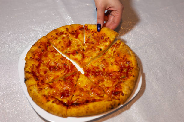 Original Italian pizza Margherita with cheese and tomato sauce on a white plate. Woman taking a slice of pizza