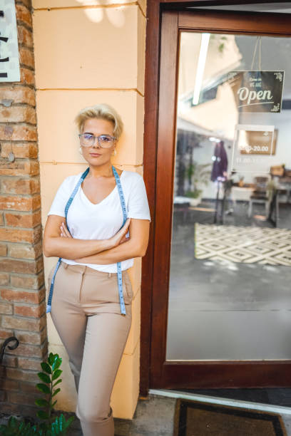 Adorable woman waitress or bartender wearing blue casual shirt and beige apron, smiling a toothy smile, holding out a disposable eco paper bag with fresh delivered food, isolated over white background