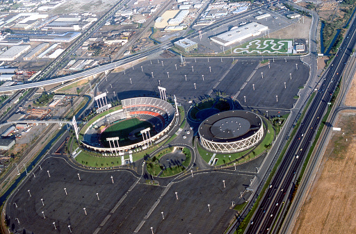 Oakland, California, USA - July 1978: Aerial view of Oakland-Alameda County Coliseum Complex including the Oakland Coliseum, Oakland Arena. The coliseum is used for both football and baseball. The arena is used for basketball. Special events are held in both venues. Interstate 880 is to the right, BART (Bay Area Rapid Transit) is to the left.