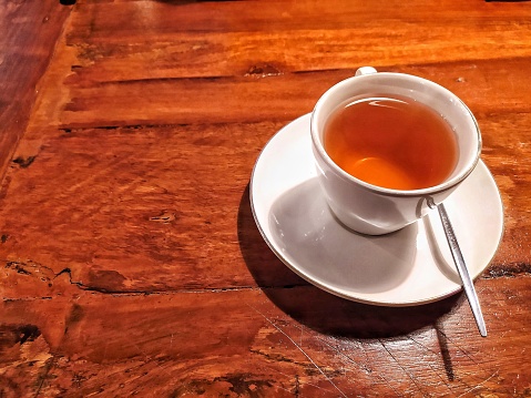 A cup of tea with metal spoon above wooden desk