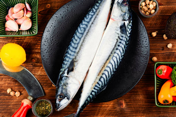 Raw mackerel fish, Scombrus with herbs and spices on wooden board. Orange background. Top view. Copy space.