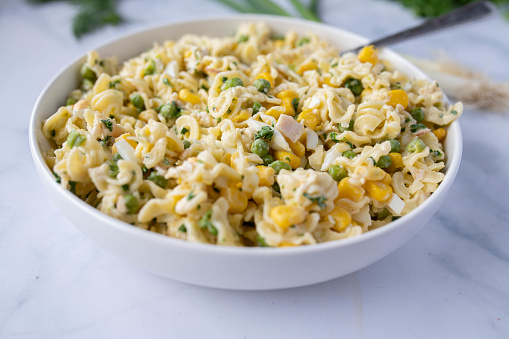 Low fat and high protein pasta salad with chicken breast, geen peas, corn and herbs in a bowl isolated on kitchen counter. Closeup