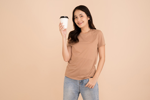 Happy young woman holding coffee cup standing in the studio brown background
