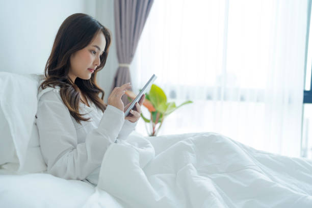 istock Girl lying in bed playing tablet computer in bedroom 2147689482