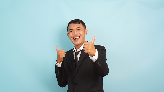 Joyful male executive showing approval with enthusiastic thumbs up, against a blue background