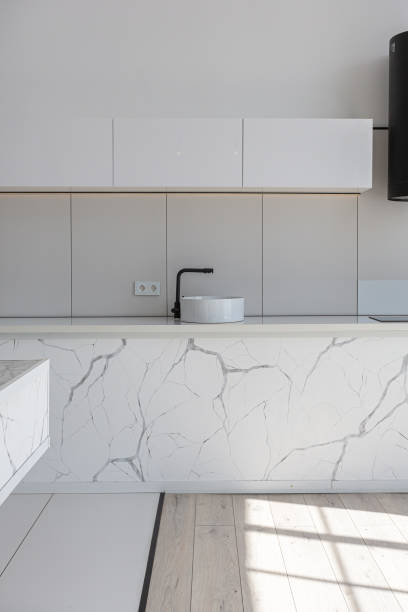istock kitchen and dining island with high bar stools in a minimalistic modern luxury design of an expensive house on a sunny day. white walls with plaster, parquet, decorative lighting and no one inside 2147690409