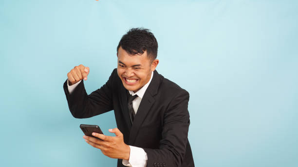 istock Angry Asian executive with unhappy expression pointing phone, in formal attire, light blue backdrop 2147690825