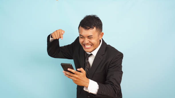 istock Angry Asian executive with Irritated expression pointing phone, in formal attire, light blue backdrop 2147690906