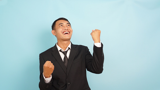 Exultant man in business attire with fists pumped, exuding confidence against a light blue background