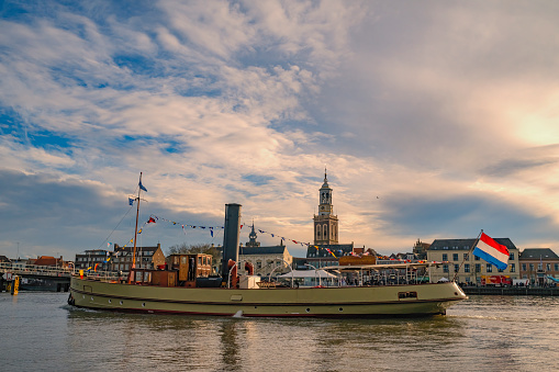 Old steam boat at the river IJssel during the 2018 Sail Kampen event in the Hanseatic league city of Kampen in Overijssel, The Netherlands. People on board are looking at the view and a crownd on the quay is watching the ships.
