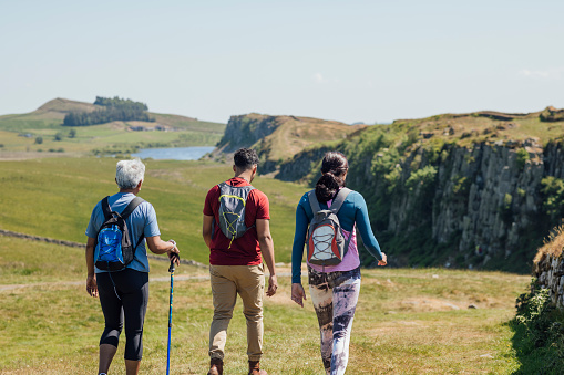 A mother and her two adult children are hiking a scenic route, crag lough can be seen in the distance. They're all wearing hiking sports attire on a summer's day at Hadrian's Wall, Northumberland.  Videos are available similar to this scenario.