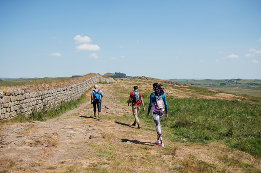 A full shot of a mother and her two adult children hiking a scenic route. They're all wearing hiking sports attire on a summer's day at Hadrian's Wall, Northumberland. Videos are available similar to this scenario.