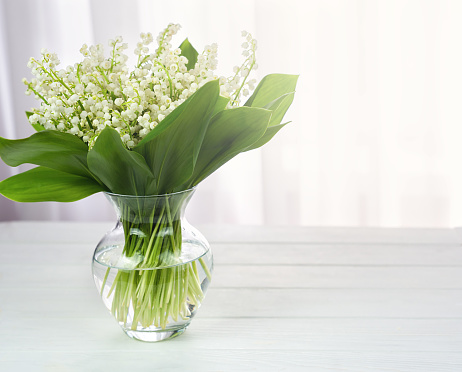 A bouquet of fresh lilies of the valley in a vase on the table. Copy space. Selective focus.