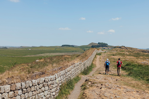 Full shot of mother and son walking alongside Hadrian's Wall, Northumbria. They are wearing casual sports clothing on a summer's day and walking off into the horizon. Videos are available similar to this scenario.