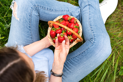 Young woman eating ripe juicy strawberries sitting on the grass outdoor. Healthy lifestyle concept. Top view. Selective focus.