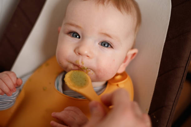 istock Cheerful baby child eats food itself with spoon. 2147693832