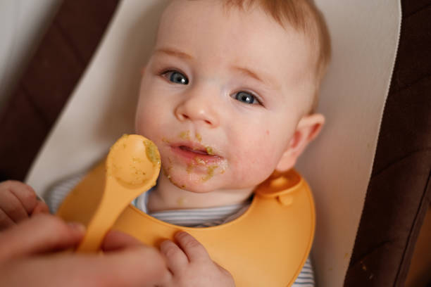 istock Cheerful baby child eats food itself with spoon. 2147693834