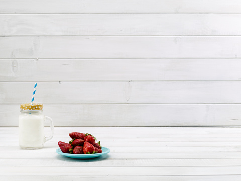 Milk and strawberries on a white wooden table