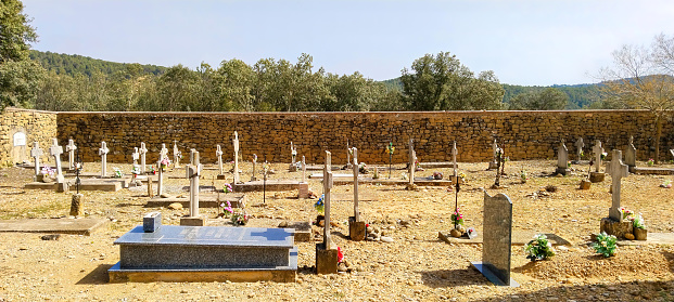 A cemetery with many graves and a large stone wall. The cemetery is empty and quiet. Scene is somber and peaceful