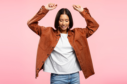 Smiling authentic Asian woman wearing casual brown shirt holding hands up isolated on pink background. Fashion concept