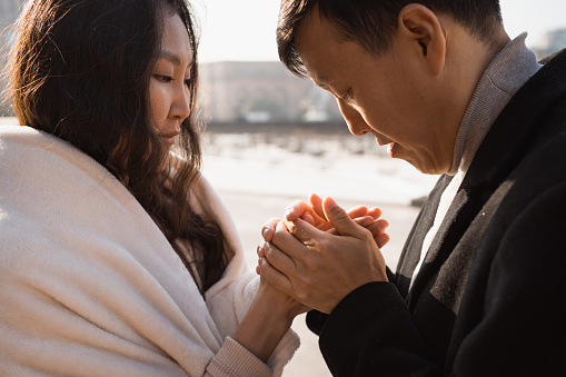 Man warms his girlfriend's hands with his own hands and breath at walk in city. Trust, care, honesty and relationship concept, close up view