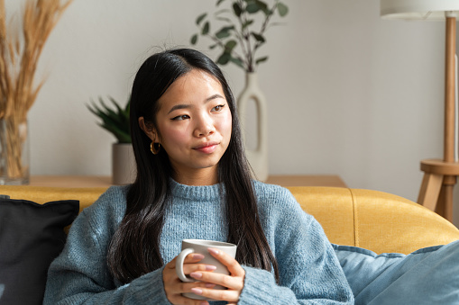 Serene young woman holds a mug, lost in thought, in a cozy home setting