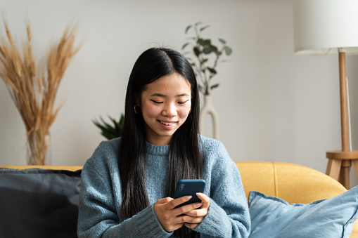 Cheerful young woman in a cozy setting using her mobile phone with a smile