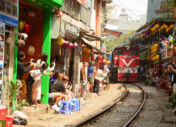 Vietnam-Hanoi / 5 march 2024 : Railway line passing between narrow buildings in the Old Quarter of Hanoi. Famous train street with locomotive and people standing next to the train tracks. Tourist attraction