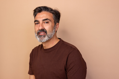 Portrait of a content middle-aged man with a grey beard and casual t-shirt on a warm background
