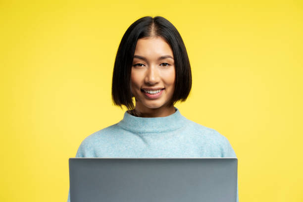 istock Smiling, beautiful Asian woman using laptop with stylish hairstyle using website looking at camera 2147697478
