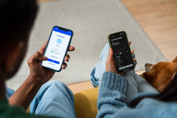 Man comparing health app and stock market on smartphones Person checks fitness progress on one phone and stock investments on another, with pet dog beside ppp-program stock pictures, royalty-free photos & images