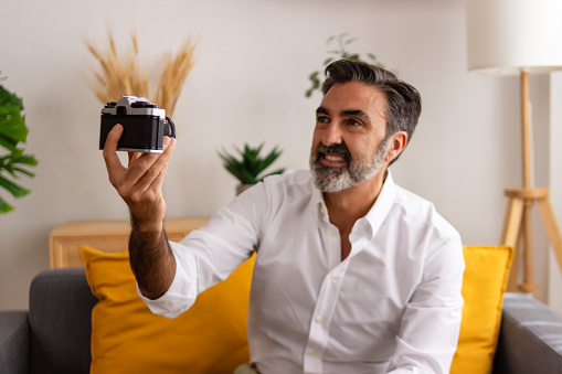Cheerful middle-aged man holding a classic camera in a well-lit living room setting
