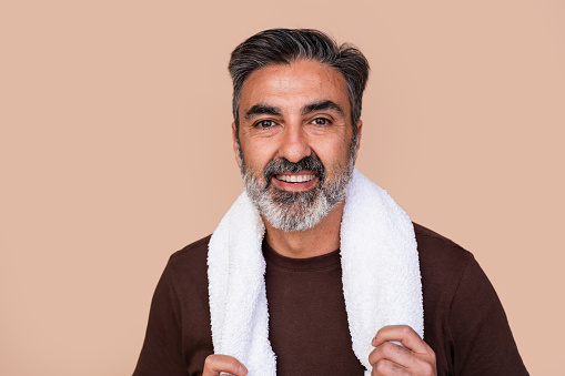 Portrait of a cheerful mature man with a white towel around his neck against a beige background