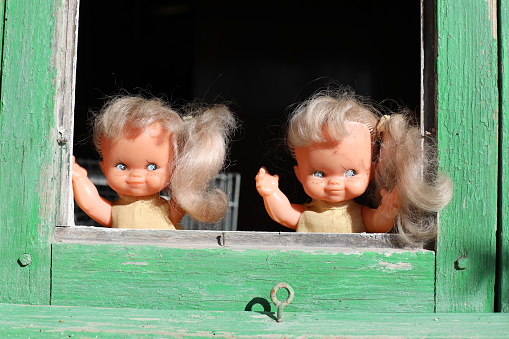 Two spooky twin sister dolls are looking through green  window. The setting is perfect to create a terrifying Halloween fantasy.