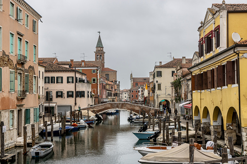 Chioggia,Veneto,Italy, March 30, 2024 : Chioggia cityscape in Venice Lagoon with narrow Vena water canal with colorful boats among old buildings