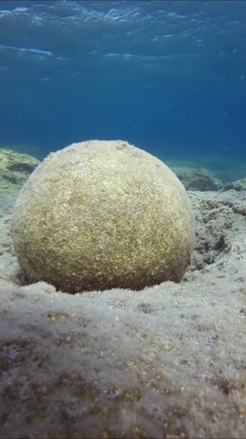Old stone cannonball lying on rocky seabed on blue water background